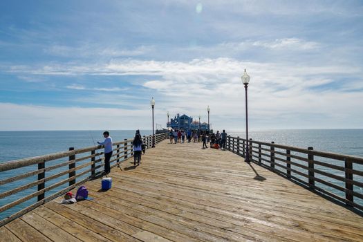 Tourist walking on the Oceanside Pier during blue summer day, Oceanside, northern San Diego County, California. Wooden pier on the western United States coastline. Famous for fisher. March 22nd, 2020