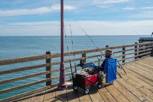 Tourist walking on the Oceanside Pier during blue summer day, Oceanside, northern San Diego County, California. Wooden pier on the western United States coastline. Famous for fisher. March 22nd, 2020