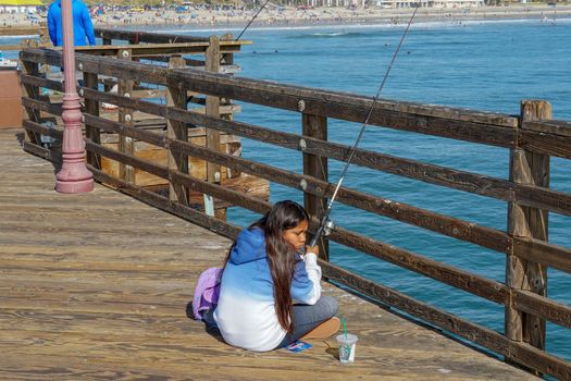 Tourist walking on the Oceanside Pier during blue summer day, Oceanside, northern San Diego County, California. Wooden pier on the western United States coastline. Famous for fisher. March 22nd, 2020