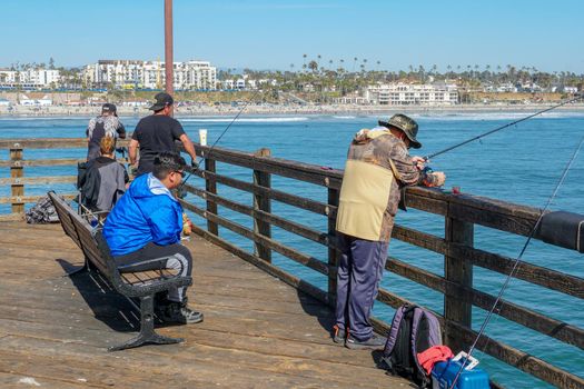 Tourist walking on the Oceanside Pier during blue summer day, Oceanside, northern San Diego County, California. Wooden pier on the western United States coastline. Famous for fisher. March 22nd, 2020