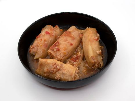 A dish of cabbage rolls in a black plate, which is minced meat with boiled rice, wrapped in cabbage leaves.