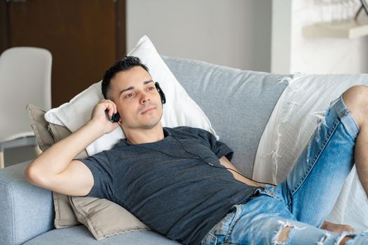 the guy enjoys the music while lying on the couch with headphones. Relaxation with music.