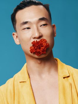 Happy male of Korean appearance on a blue background with a flower in his mouth. High quality photo