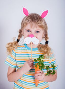 Cute little girl with bunny ears holding carrot on gray background