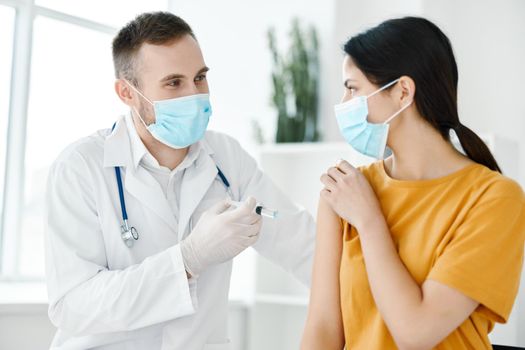 a laboratory assistant in a medical gown holds a syringe in his hand and a patient in a yellow T-shirt. High quality photo