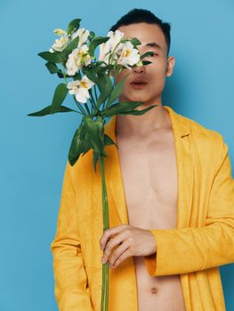 A romantic man holds a bouquet of white flowers in front of his face and a naked torso in a yellow coat. High quality photo