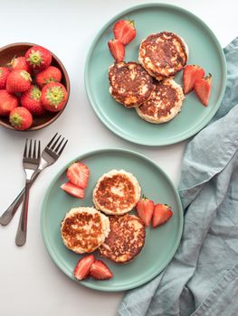 Sweet cheese pancakes on plate served strawberries. Cottage cheese pancakes, syrniki, ricotta fritters, curd fritters. Top view or flat lay. Vertical.