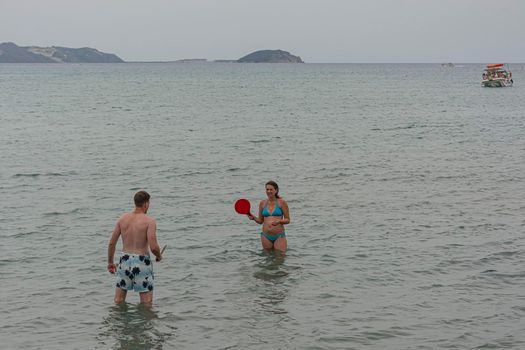 Greece, Laganas - 2016, June 19: A guy and a girl stand in the water and play ping pong, blurred background. Stock photo.