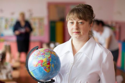 Belarus, the city of Gomel, May 10, 2019. Open day in kindergarten.Portrait of a teacher with a globe.Elderly woman teacher.