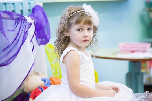 Belarus, the city of Gomil, December 27, 2018. Morning party in kindergarten.Beautiful girl in a white dress sitting. Three year old girl on holiday.