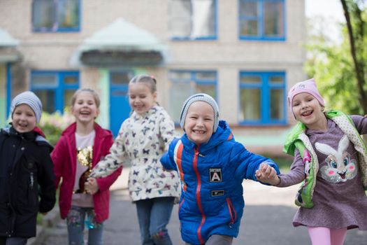 Belarus, the city of Gomel, May 10, 2019. Open day in kindergarten.Happy preschoolers on the street. Children holding hands jumping. A group of six year old friends.