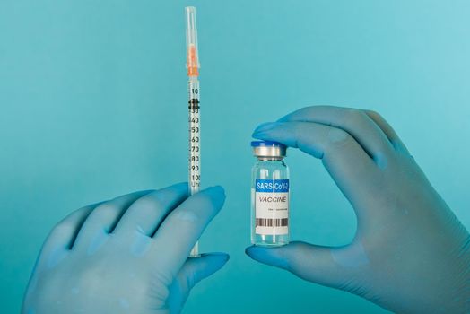 Covid-19 coronavirus vaccine bottle and syringe in womans hands on blue background. Selective focus. Close-up.