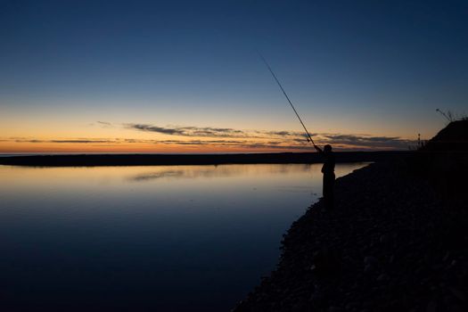 Seascape with a silhouette of a fisherman on the evening background
