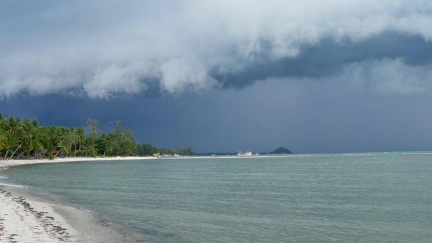Waving blue sea, sandy shore of Samui Island during wet rain season, Thailand. Hurricane and storm warning on exotic tropical ocean beach. Fast wind and ominous clouds. Danger typhoon thunderstorm.