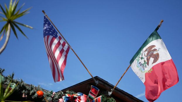 Mexican tricolor and American flag waving on wind. Two national icons of Mexico and United States against sky, San Diego, California, USA. Political symbol of border, relationship and togetherness.
