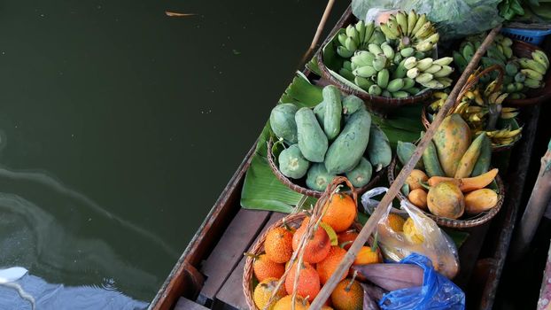 Iconic asian Lat Mayom floating market. Khlong river canal, long-tail boat with tropical exotic colorful fruits, organic locally grown vegetables. Top view of harvest and street food in wooden canoe.