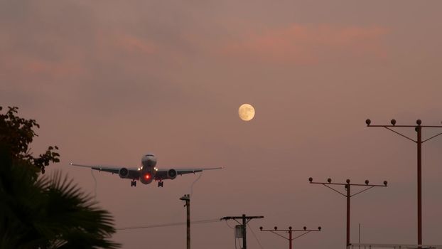 Airplane landing in LAX airport at sunset, Los Angeles, California USA. Passenger flight or cargo plane silhouette, dramatic cloudscape. Aircraft arrival to airfield. International transport flying.