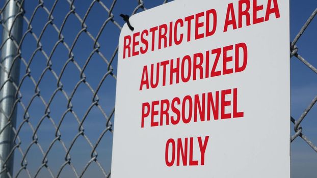 Restricted area, authorized personnel only sign in USA. Red letters, keep off warning on metal fence, United States border symbol. No trespassing notice means violators will be prosecuted by US law.