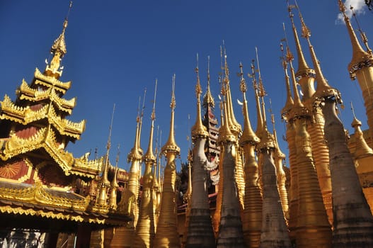 Exterior of exotic temple with stupas and payas, From below shot of golden bright stupas of temple on lake Inle under blue sky, Myanmar. Sacred place.