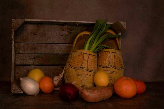 still life with a wooden box with old dutch worn out wooden shoes and various fruits