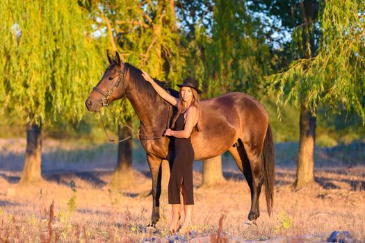 A girl hugs a horse against a background of trees, the rays of the setting sun fall on them