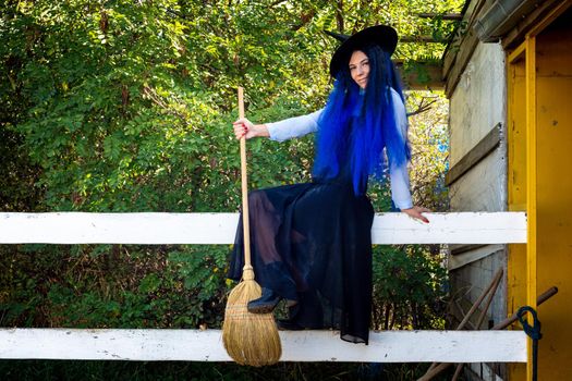 Beautiful girl in a witch costume sits on the fence