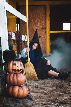 A girl dressed as a witch with a broom squatted by the fence at the Halloween celebration