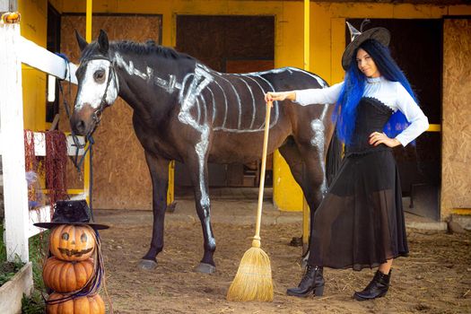 A witch on a farm stands next to a horse and an evil pumpkin man