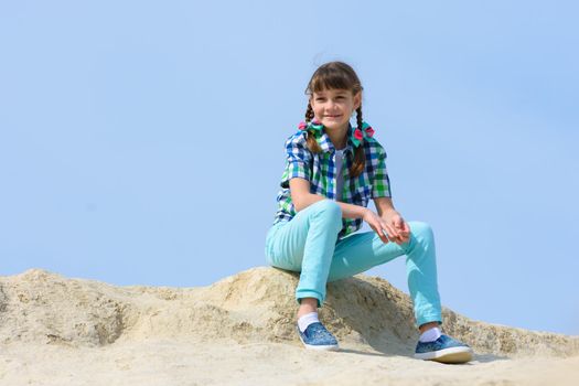 A ten year old girl sits on a hilltop and smiles