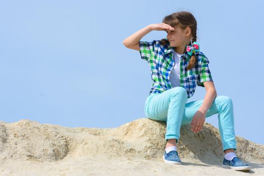 The girl sits on the top of the hill and looks into the distance