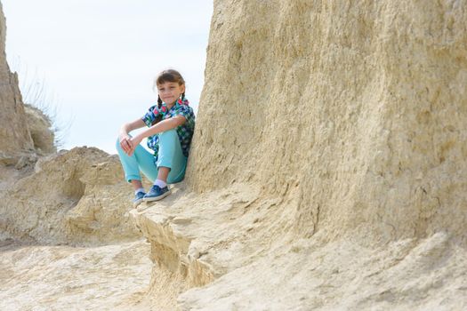 Girl in casual clothes sits on a cliff ledge