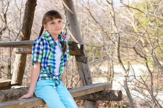 A girl sits on a wooden bench in the forest on a warm autumn day and looks into the distance