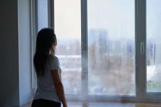 Cold winter weather. Woman step to window, open it and frosty air rushes from outside through open windows to apartment. Airing housing in cold winter.