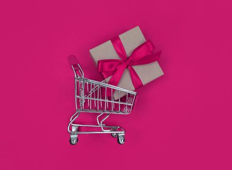 Supermarket trolley and gift box on a pink background. Shopping concept.