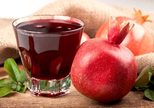 Garnet juice in a glass and pomegranate on wooden boards, on natural fabric