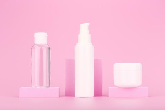 Set of cosmetic bottles on pink podium against pink background. Cleansing lotion, face cream and under eye gel for daily skin care. Concept of beauty routine