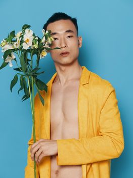 Sexy man with a naked body on a blue background and a yellow coat with a bouquet of flowers in the holidays gifts. High quality photo