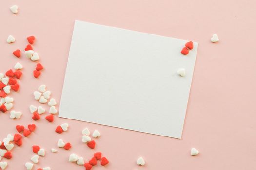 Valentine's Day background with red and white little hearts, empty white greeting card on pink backdrop. Valentines day concept. Copy space. Top view. Mockup