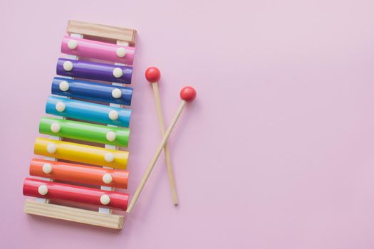 Rainbow Colored Wooden Toy Xylophone on pink bacground. Glockenspiel toy made of metal and wood. Top view. Free space for text