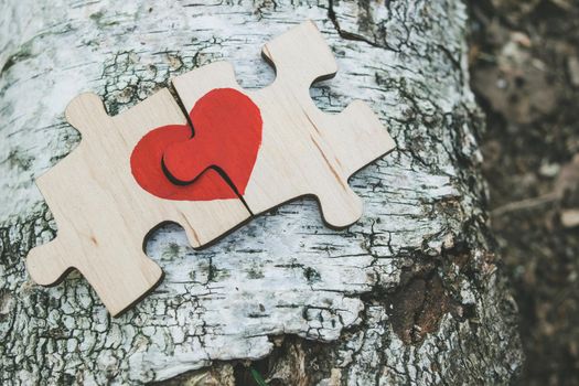 Red heart is drawn on the pieces of the puzzle lying next to each other on wooden background. Love concept. St. Valentine day