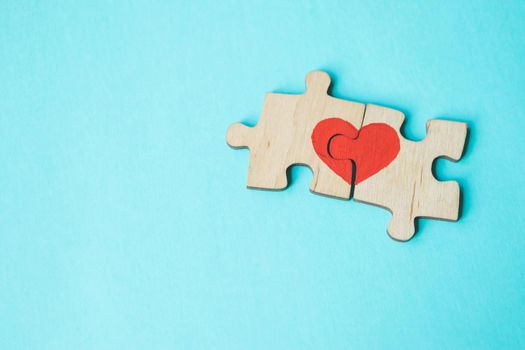 Red heart is drawn on the pieces of the wooden puzzle lying next to each other on blue background. Love concept. St. Valentine day. Reconciliation. Reunion concept. Free space for text