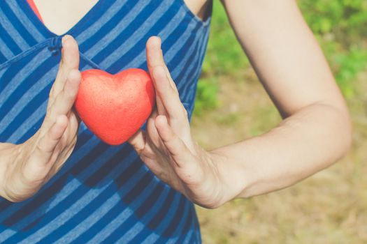 people, relationship and love concept - womans hands holding red heart on green background
