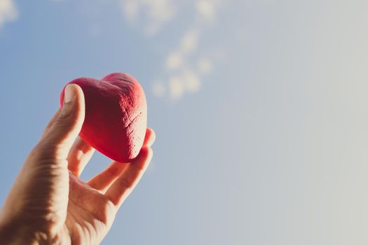 Hand holding the red decorative heart against the blue sky. Day of donor. Love concept. Copy space