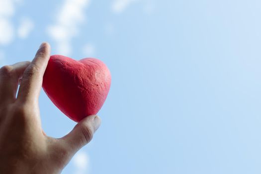 Hand holding the red decorative heart against the blue sky. Day of donor. Love concept