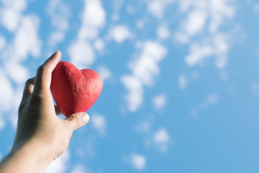 Hand holding the red decorative heart against the blue sky. Day of donor. Love concept