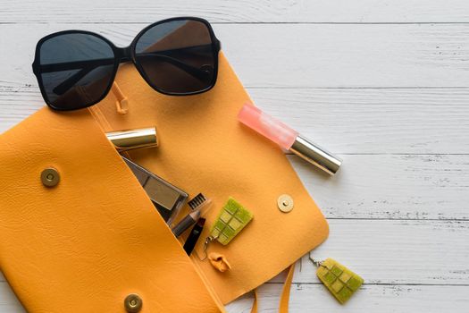 Female things and orange handbag on white wooden background with copyspace. Cosmetic products, sunglass, earrings. Flat lay, top view. Fashion concept