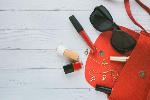 Female things and red handbag on white wooden background with copyspace. Cosmetic products, sunglass, earrings. Flat lay, top view. Fashion concept.