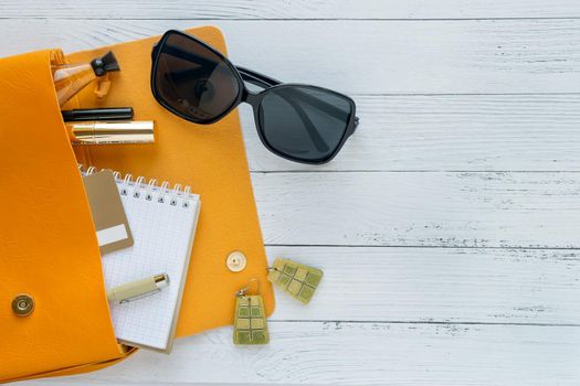 Female things and orange handbag on white wooden background with copyspace. Cosmetic products, sunglass, notebook. Flat lay, top view. Fashion concept