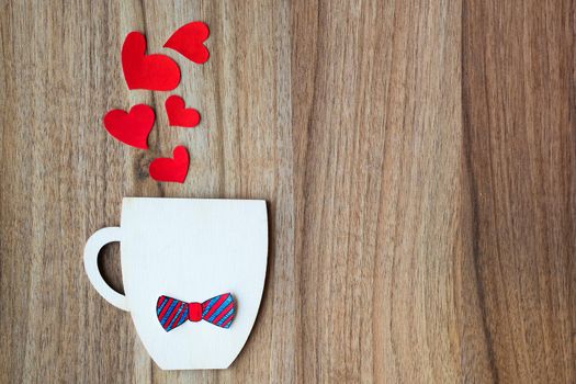 Decorative Cup with bow-tie and hearts on wooden background. Greeting card