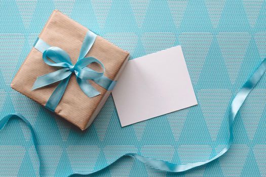 Gift box with blue ribbon on blue background wih greeting card.